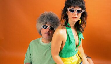 Photo of a woman sitting on a man's lap against an orange backdrop