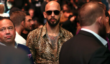 A bald man wearing sunglasses and a leopard print button down shirt.