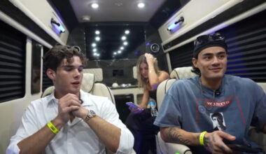 Clavicular sits on the left in a sprinter van. He is wearing a white-button down shirt. He is seated next to another man wearing a blue t-shirt. There is woman sitting behind them.