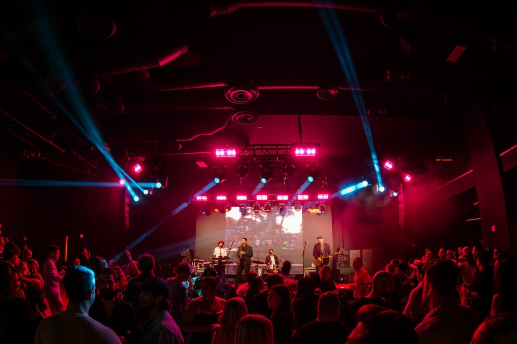 Photo of a band performing on stage in front of a crowd. 