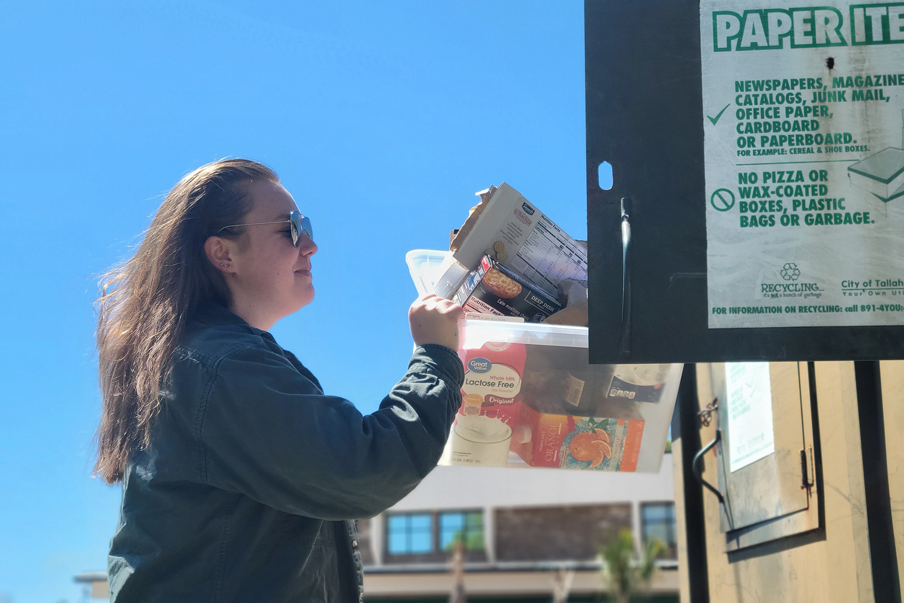 Close-up of a Tallahassee city recycling bin for paper products, showing a person emptying a bin of assorted cardboard packaging.