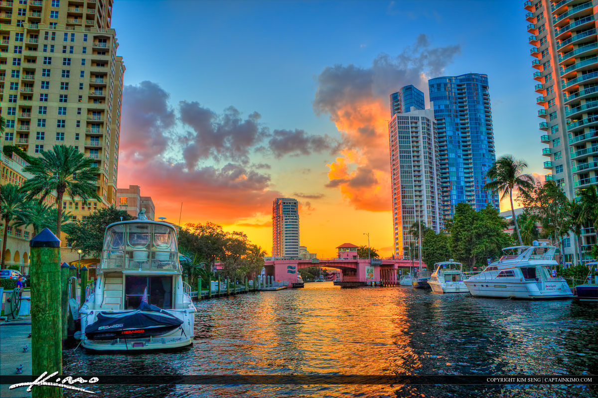 an orange sunset behind skyscrapers and a riverwalk
