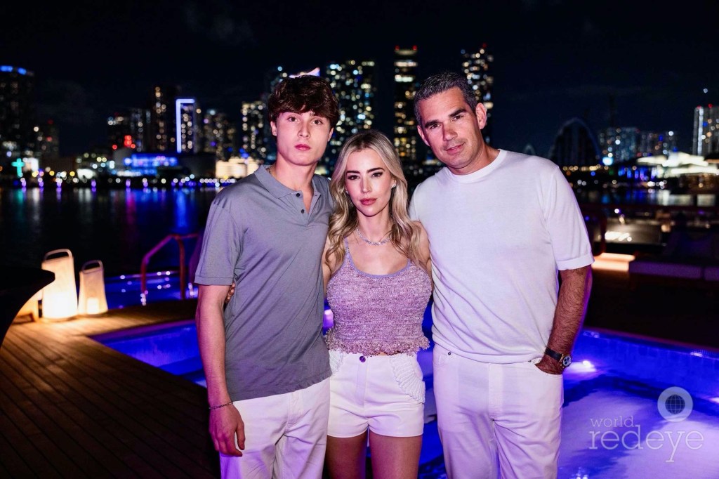 photo of a man, woman, and young man posing in front of a boat and the Miami skyline