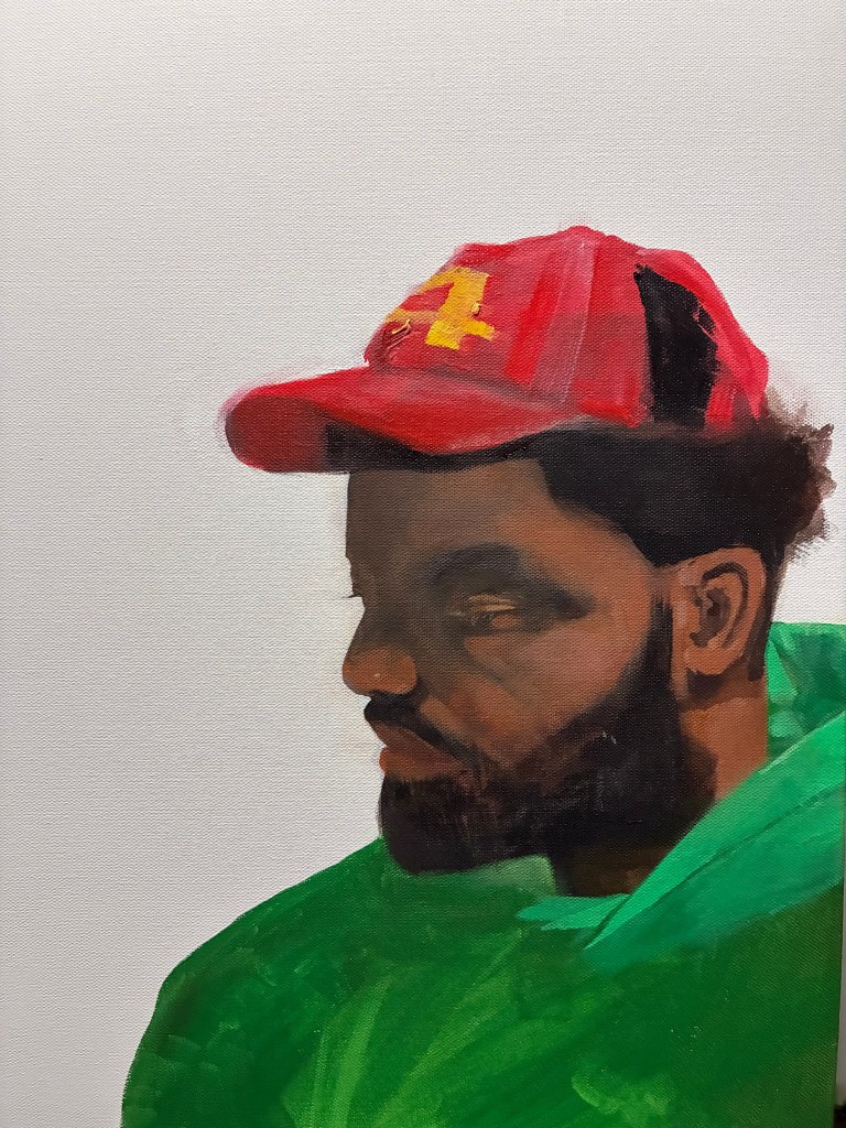 A profile painting of a person with a dark beard and a red baseball cap, looking downward with a contemplative expression. They are wearing a bright green garment, rendered in expressive brushstrokes against a plain white canvas background.