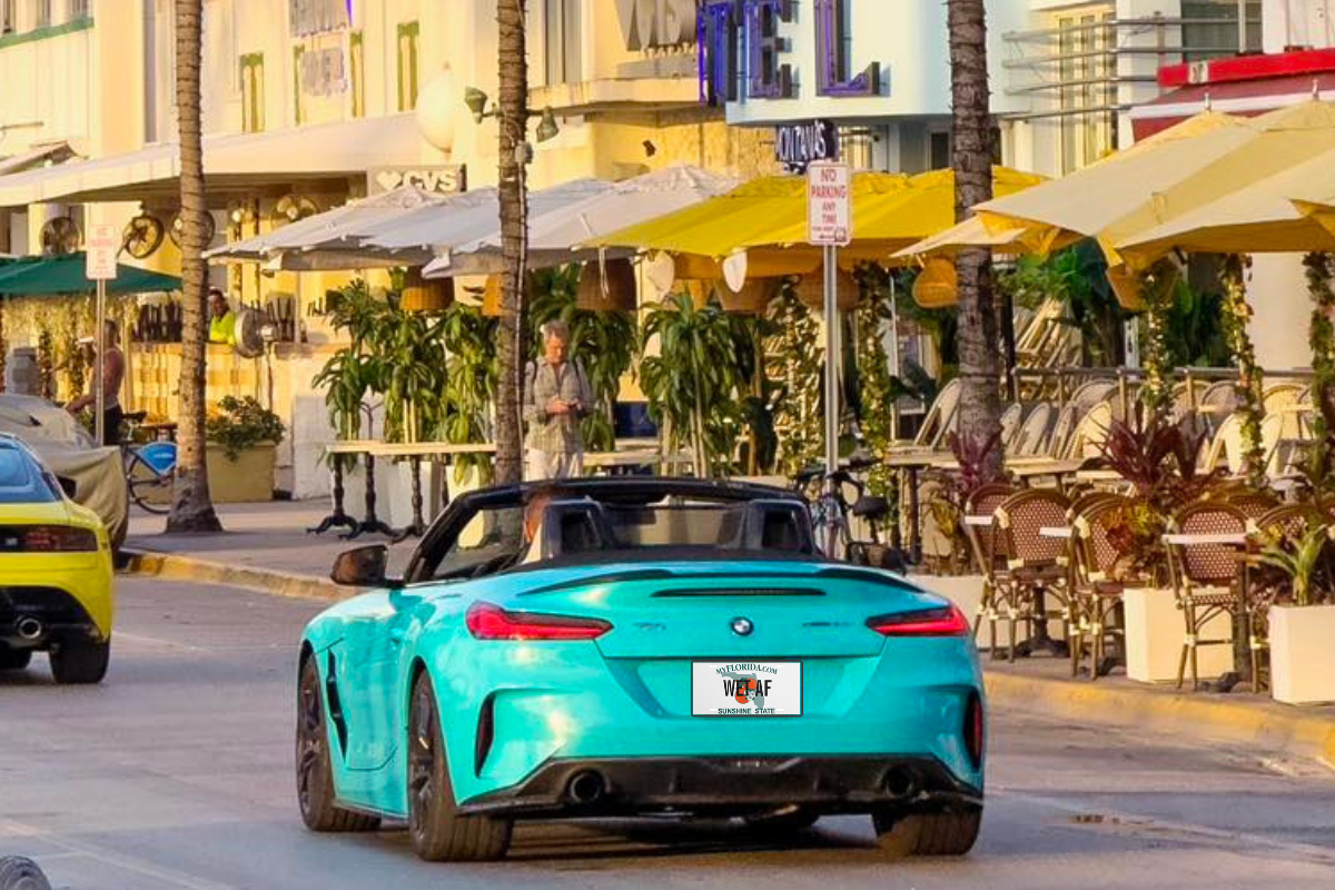 Teal BMW convertible on Ocean Drive with a Florida license plate that says "Wet AF."