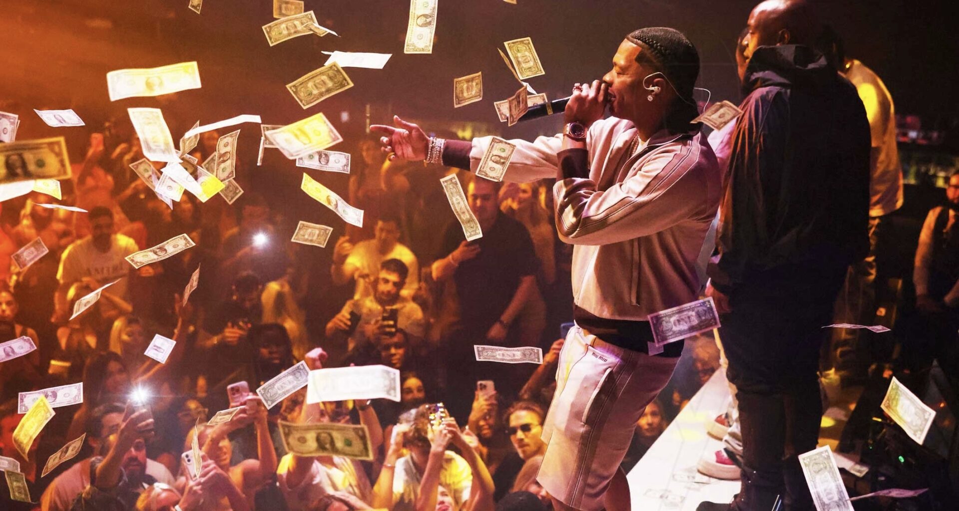 photo of rapper Lil Baby performing onstage at a club as dollar bills rain down around him