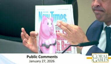 Commission meeting screenshot of Mayor Lago holding the cover of Miami New Times with four fingers. You can only see the bottom half of his face including his mouth and nose. The cover shows an angry pig wearing a bra and underwear.