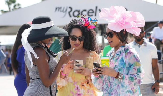 Daveeka Burns, left, Nefertiti Thomas, center, and Dr. Tanda Mercer look at their phones between races at the Pegasus World Cup day horse races, Saturday, Jan. 27, 2024, at Gulfstream Park in Hallandale Beach, Fla. (AP Photo/Wilfredo Lee)