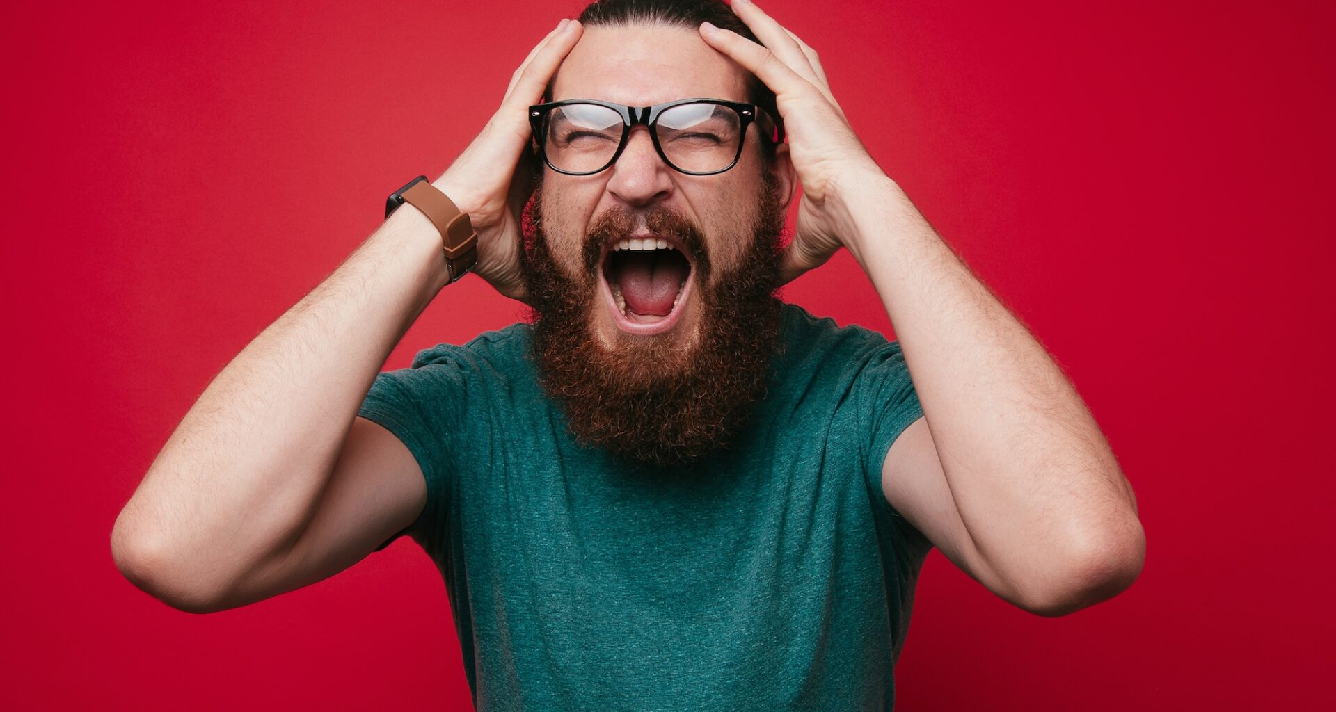 photo of a screaming bearded man looking at the camera with hands on his head
