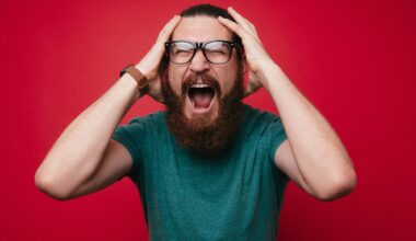 photo of a screaming bearded man looking at the camera with hands on his head