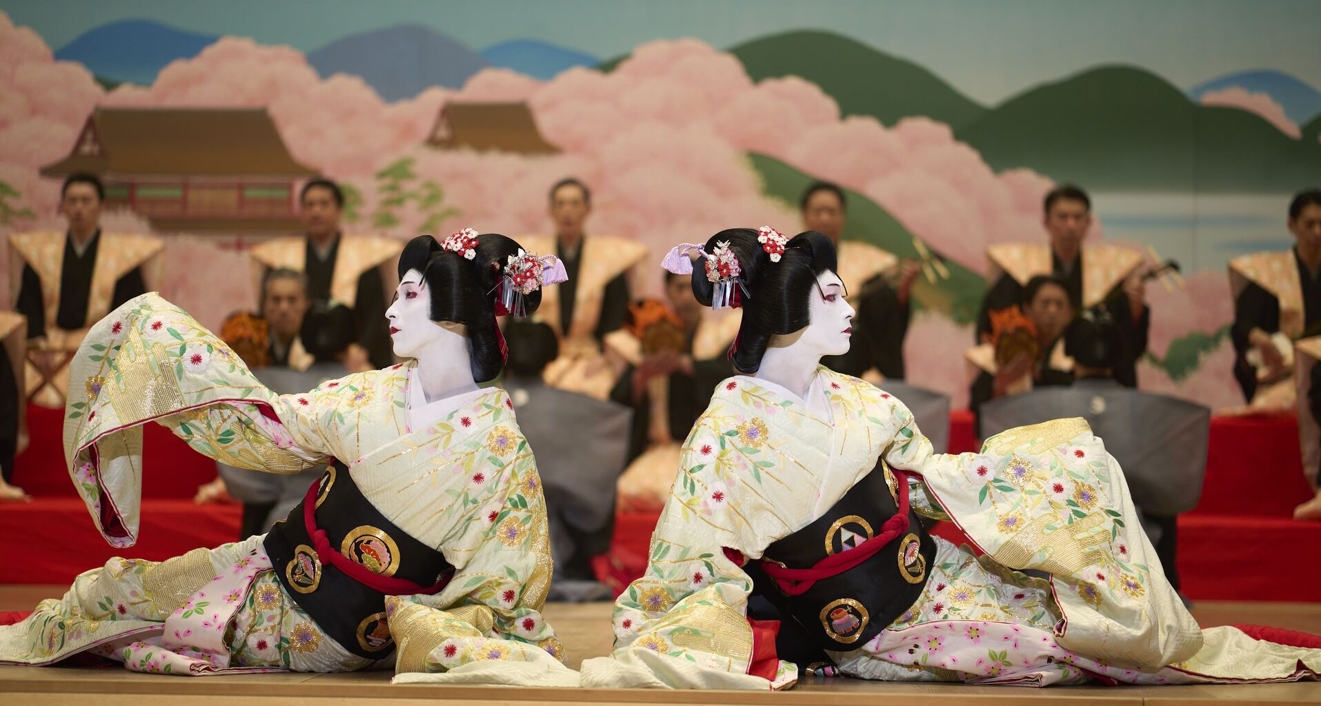 film still showing two geishas on a stage in front of men in uniforms