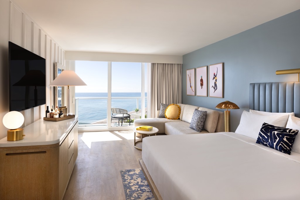 photo of a hotel room with a TV, bed, couch, and ocean view
