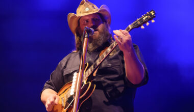 A country singer on stage wearing a cowboy hat and playing the guitar.