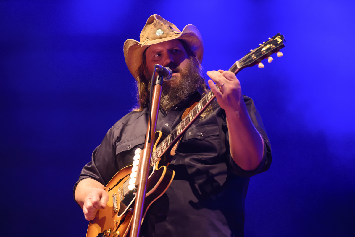 A country singer on stage wearing a cowboy hat and playing the guitar.