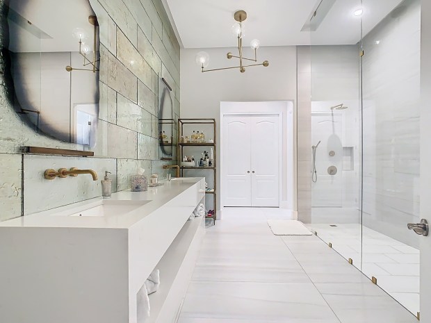 The primary bathroom has a gigantic, walk-in shower with multiple rainhead faucets. The opposite wall features an oversized vanity and designer glass tile. (Photo by Tyto Media)