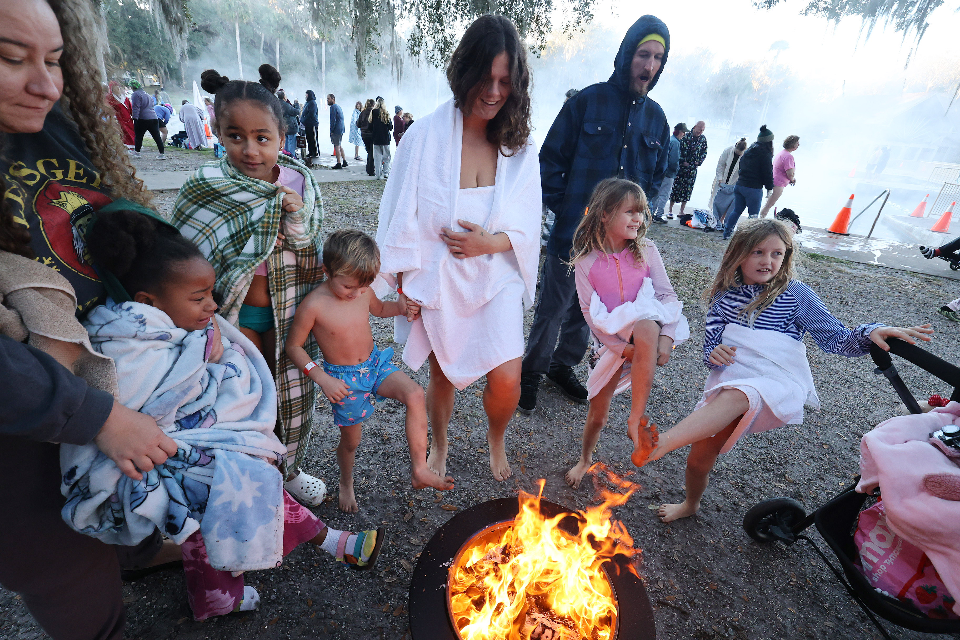 Kids and adults warm their feet by a fire pit...