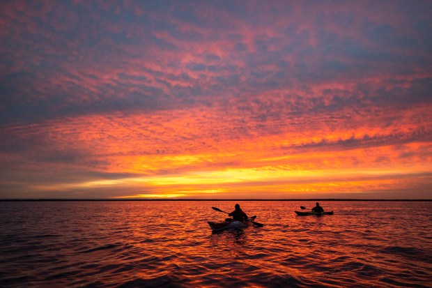 DAY 6: Greg Pflug, center, and Fred Goebel, right, are silhouetted by a vibrant sunrise over Lake George in Ocala National Forest during a kayak trip on the St. Johns River on Jan. 3, 2024. (Patrick Connolly/Orlando Sentinel)