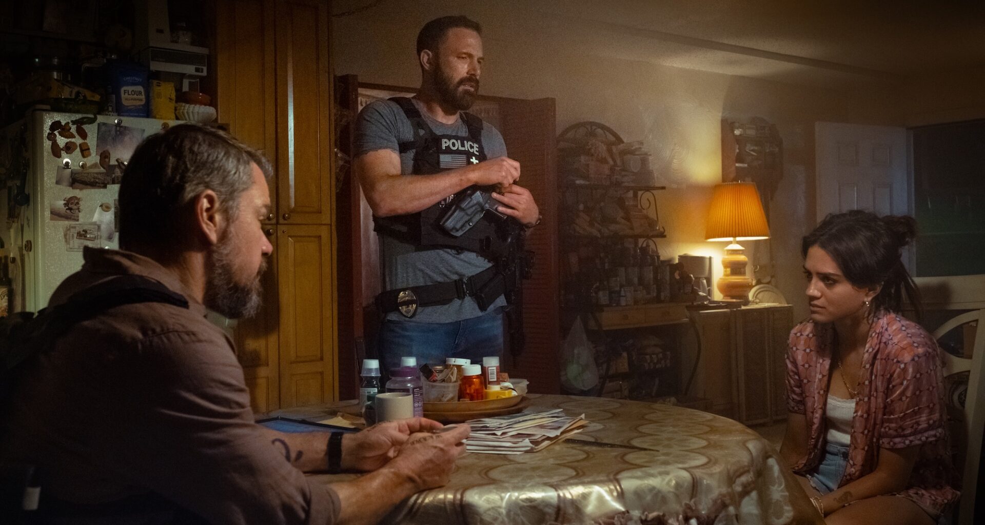 film still of two people at a dining room table speaking to a police officer
