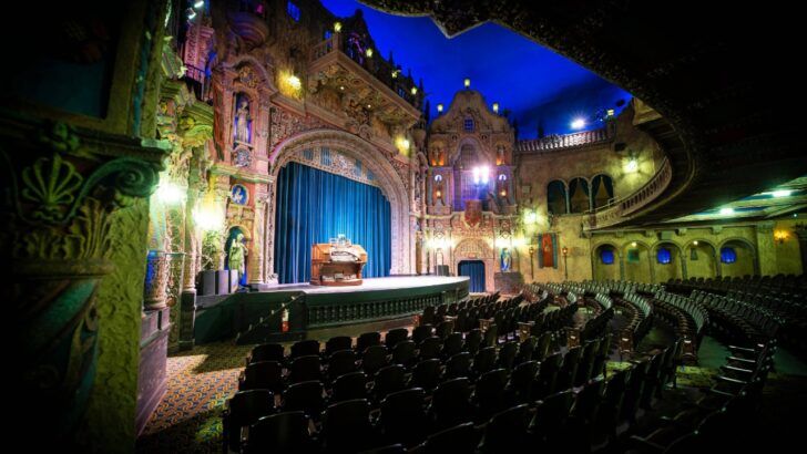 Modern interior of Tampa Theatre showing the ornate stage, blue ceiling lighting and restored seating during a performance setup.