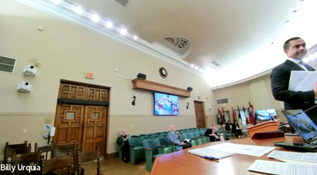 Camera footage showing Vince Lago leaving his seat with a binder in his hand standing in the commission chambers.