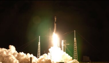 a white and black rocket lifts off into the night sky, its bright yellow-white plume lighting its launch pad below.