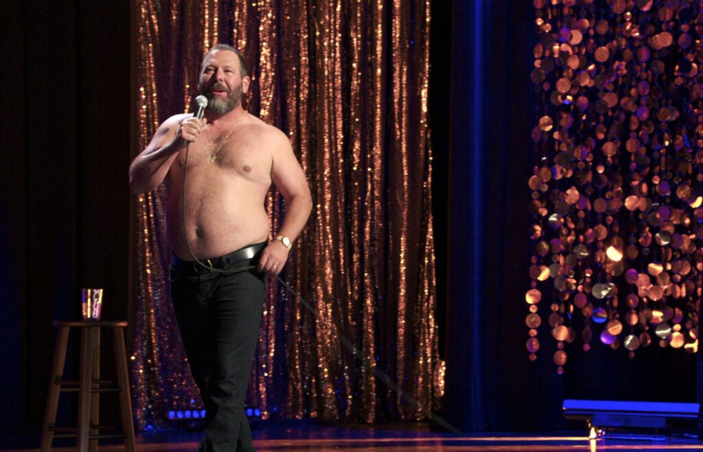 Comedian Bert Kreischer performing stand-up shirtless on stage during a Netflix comedy special.