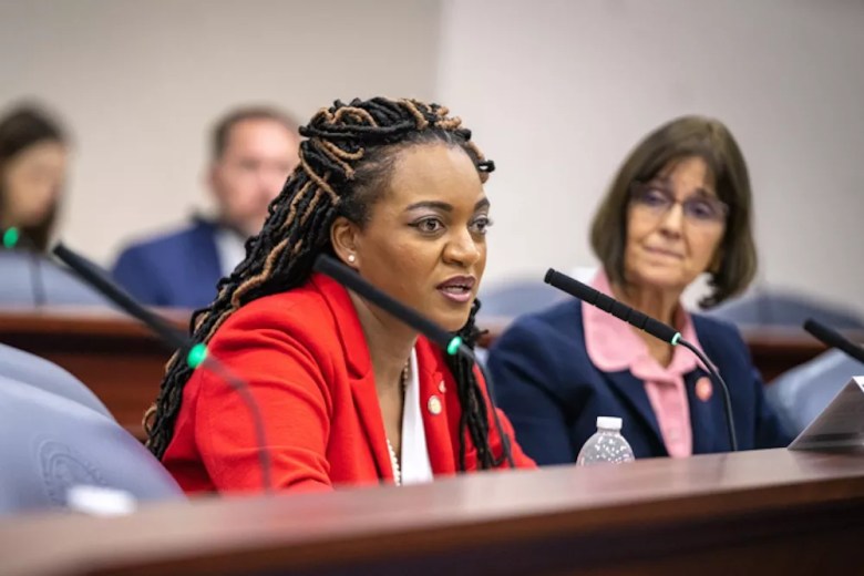 Fentrice Driskell speaks into a microphone at a desk while other House members look on. 