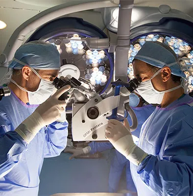Two physicians in surgical garb looking through an instrument