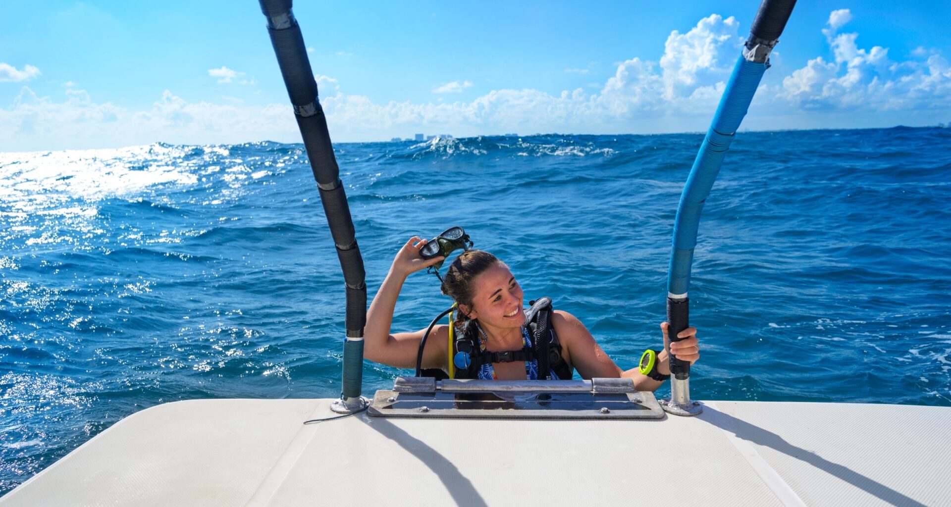 A woman smiles as she takes off her snorkeling mask while climbing aboard a boat.