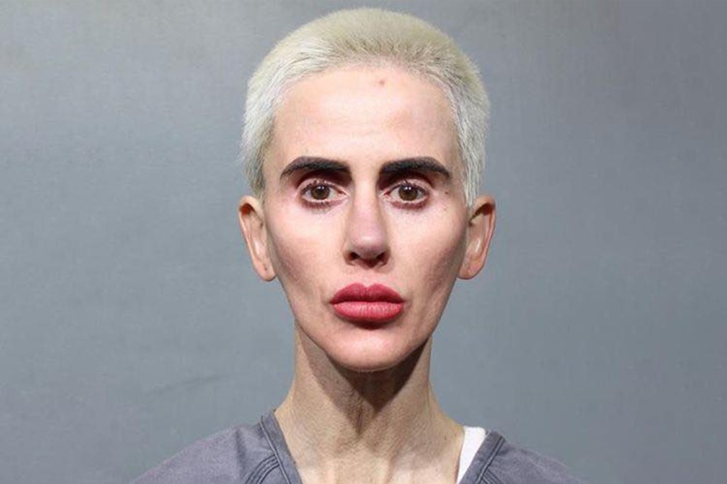 Mugshot of a woman with short, bleached blonde hair, prominent dark eyebrows, and red lipstick, looking directly at the viewer.