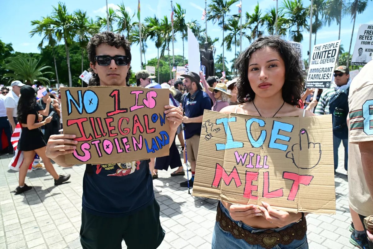 two protesters hold up painted signs reading "no 1 is illegal on stolen land" and "ICE will melt"