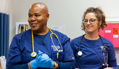 male and female nursing students wearing blue scrubs, stethoscopes and blue medical gloves