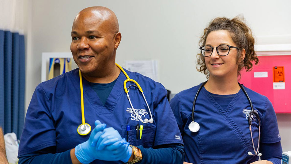 male and female nursing students wearing blue scrubs, stethoscopes and blue medical gloves