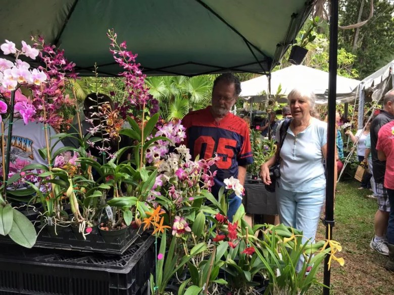 Two white people looking at orchids amid a busy plant festival.