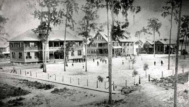 This photograph is one of the earliest taken of the Rollins College campus in 1888. The main buildings, from left, are Knowles Hall, Pinehurst Cottage and the dining hall. In the background to the left stands the home of Professor John Ford. The fence around the campus was constructed to keep grazing cows out or so the legend says. (Rollins College Archives)