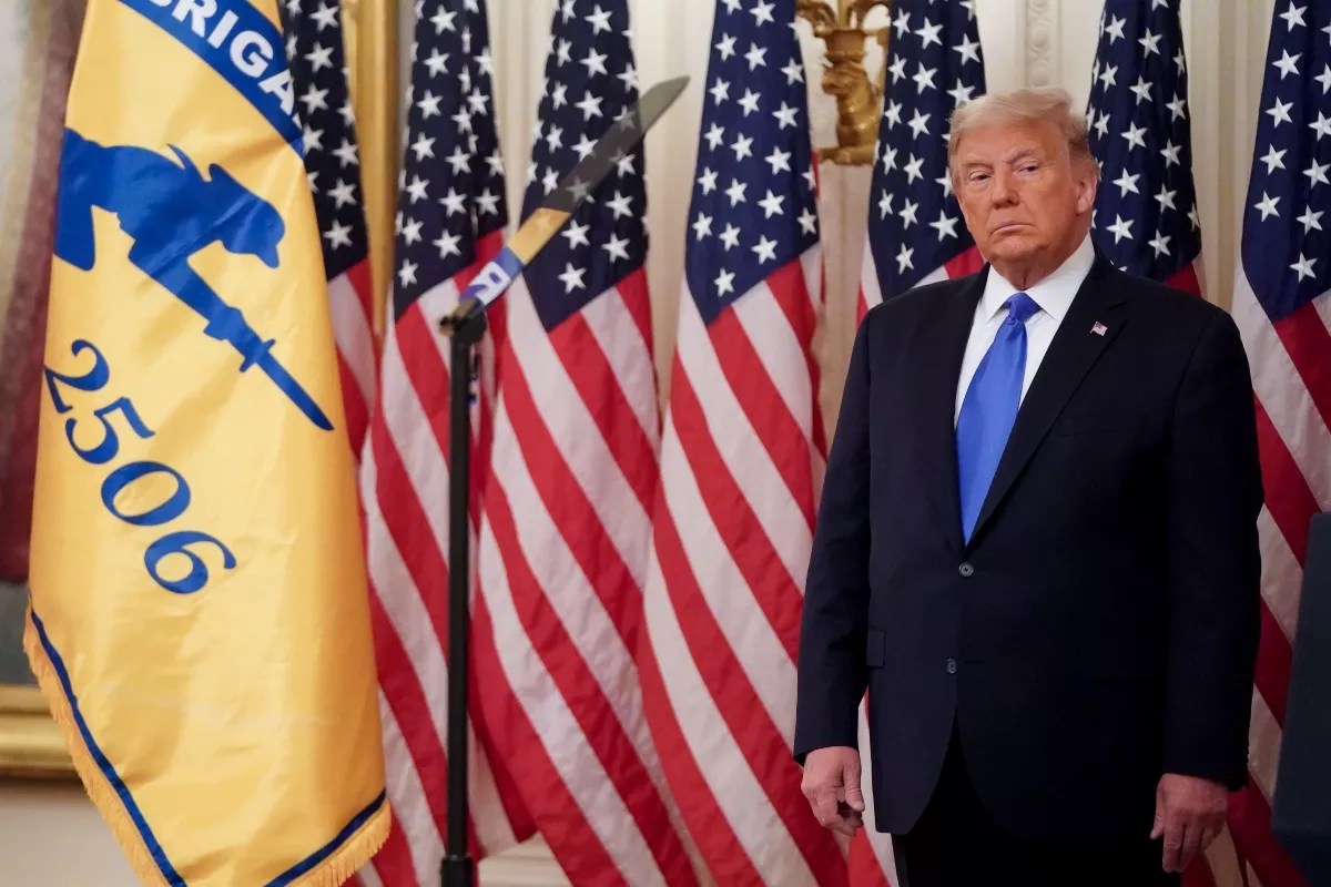 President Donald Trump stands in front of a lineup of American flags.