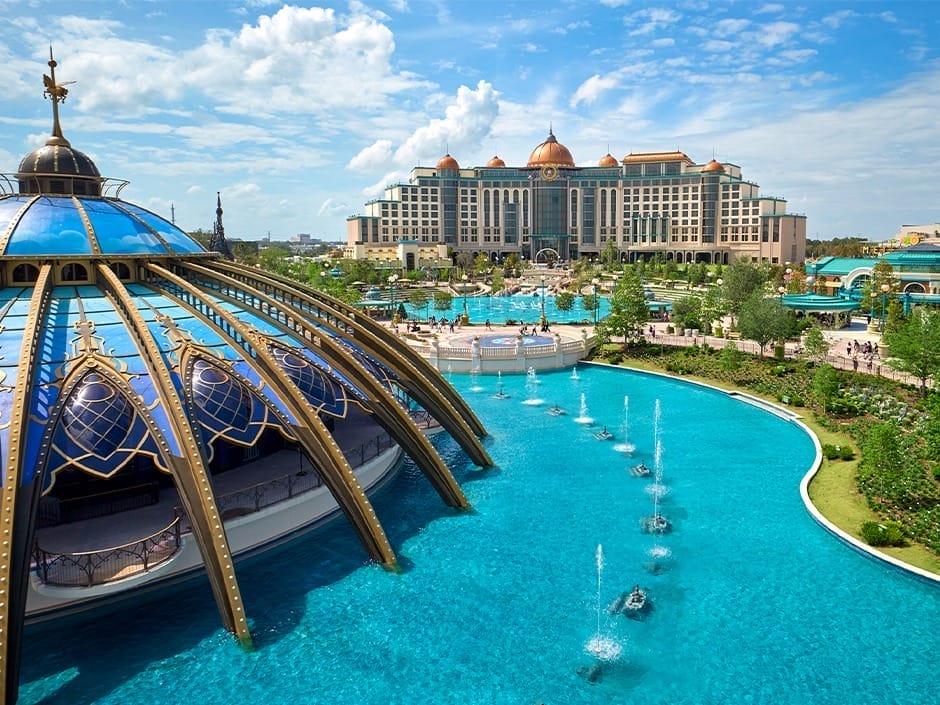 A grand hotel with domes, evoking EPCOT’s luxe resorts, overlooks a pool and pavilion—not unlike Disney castles