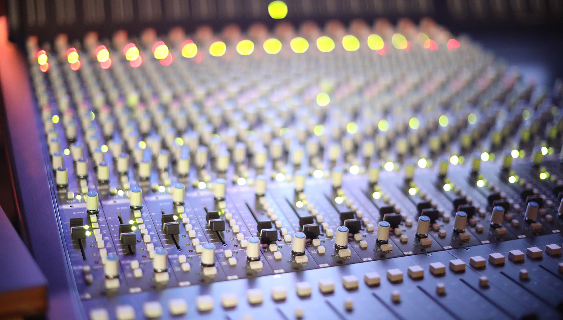 A professional music mixing console with numerous knobs and glowing indicator lights in a recording studio.