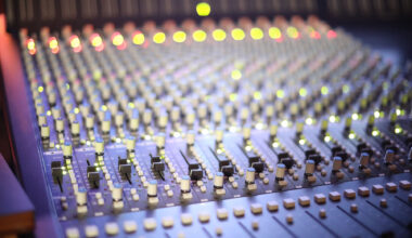 A professional music mixing console with numerous knobs and glowing indicator lights in a recording studio.