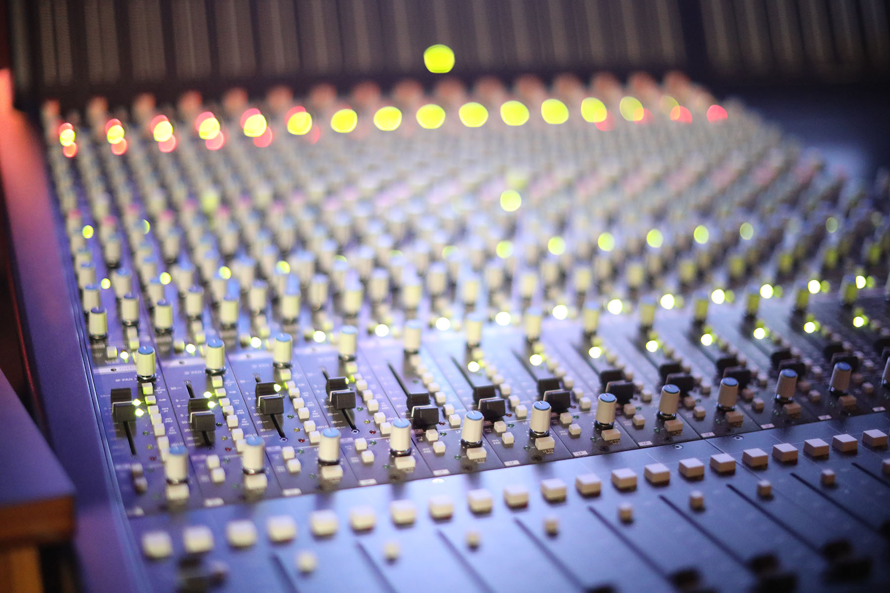 A professional music mixing console with numerous knobs and glowing indicator lights in a recording studio.
