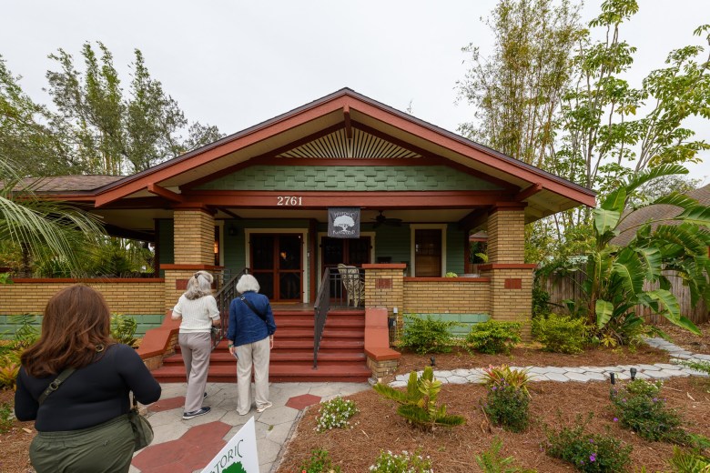 Historic Kenwood home tour attendees visiting a renovated craftsman bungalow with green siding and brick porch columns.