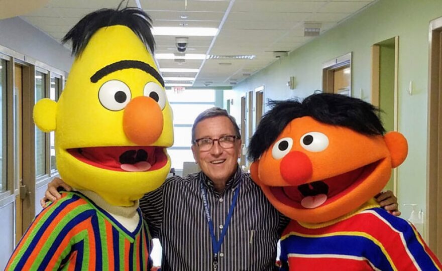 man stands between Sesame Street characters Bert and Ernie