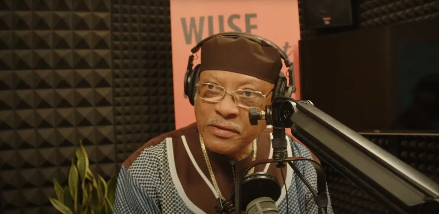 African American man wearing glasses speaks into microphone in studio
