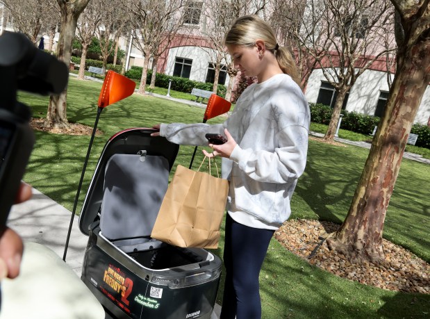 Nova Southeastern University freshman Christel Salazar picks up her food delivery from an autonomous robot on campus in Davie, Tuesday, Feb. 3, 2026. (Carline Jean/South Florida Sun Sentinel)