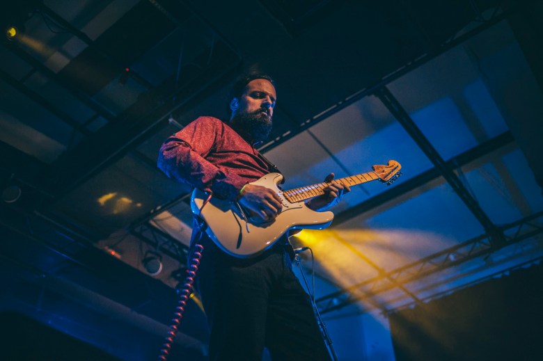 Tampa Bay area blues guitarist Power Jimi performing live on stage with a white electric guitar under dramatic blue and yellow stage lights.