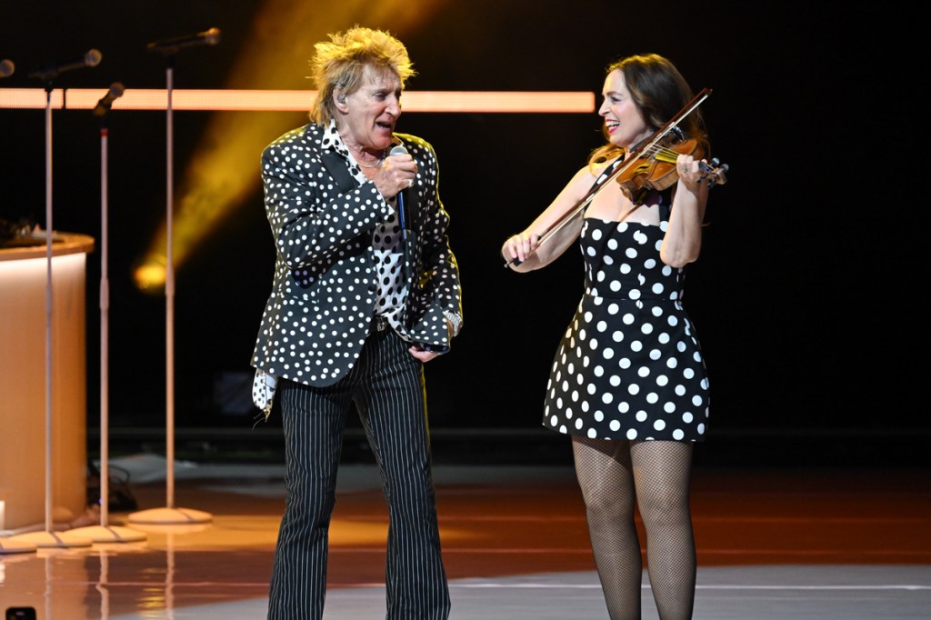 Photo of a man singing on stage next to a woman playing violin 