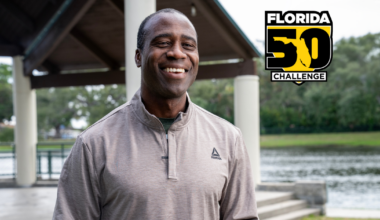 A smiling Black man in a Reebok quarter-zip shirt stands outdoors with a lake and pavilion in the background. A 'Florida 50 Challenge' logo is in the upper right.