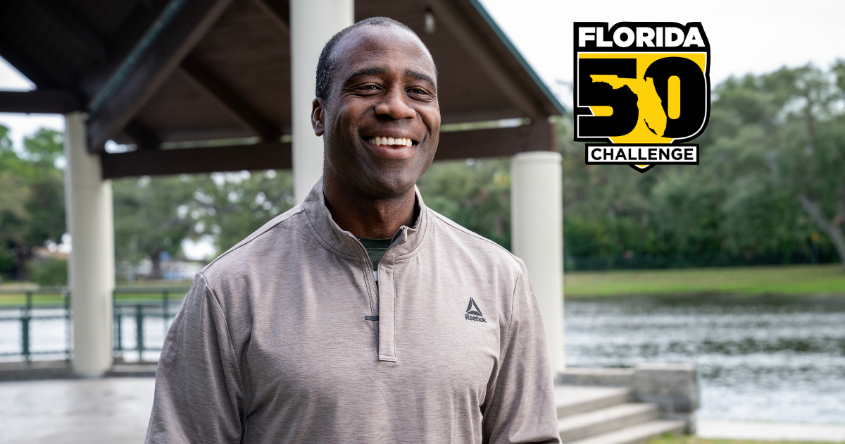 A smiling Black man in a Reebok quarter-zip shirt stands outdoors with a lake and pavilion in the background. A 'Florida 50 Challenge' logo is in the upper right.