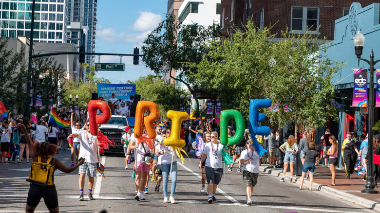 A group of people walking down the street holding PRIDE balloons
