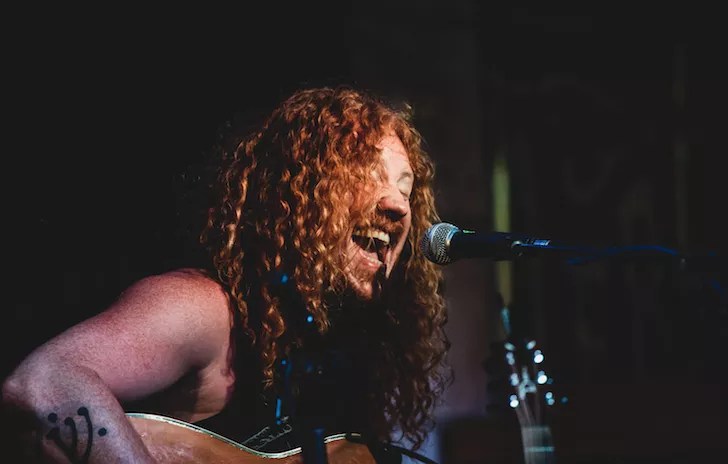 St. Petersburg musician Mountain Holler (Mark Etherington) singing passionately into a microphone while playing acoustic guitar during a live performance.